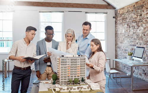 A diverse team of architects working on a building model together inside the office. A group of engineers planning a reconstruction or design project of an apartment block with blueprint documents photo