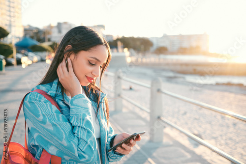 Young, stylish and elegant woman browsing phone on a beautiful day. Peaceful, stressless and smiling female on a beach front with a scenic view. Calm lady feeling happy to be outside in the city. photo