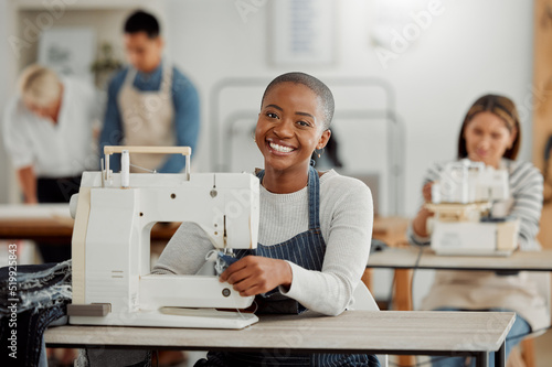 Portrait of happy black fashion designer working on clothes in a workshop. Diverse group of students doing an internship at a clothing factory, learning about the industry and how to sew on machine