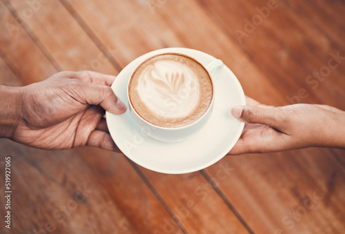 Service, customer and serving coffee to a cafe client and giving a cup of hot and fresh drink with milk foam at coffeeshop. Closeup of hands holding cappuccino with beautiful cream of latte art