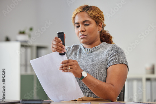 Female office worker stapling paper together in her office at work, being efficient, organized and neat. Young female admin clerk sorting and filing paperwork while sitting and working at her desk