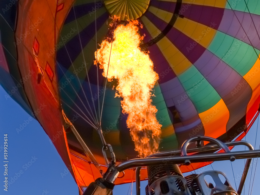 Obraz premium Hot air balloon burner flame fires into canopy as balloon floats through sky.