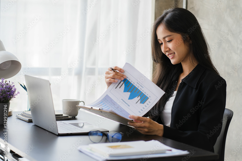 Happy Asian businesswoman using laptop computer while doing financial work. Successful with financial documents on the table Happy Asian businesswoman using laptop computer while doing financial work. Successful with financial documents on the table
