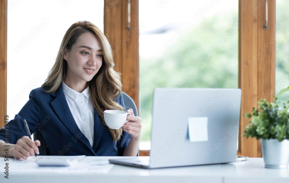 Beautiful young Asian businesswoman drinking a coffee working on laptop at office. Beautiful young Asian businesswoman drinking a coffee working on laptop at office.