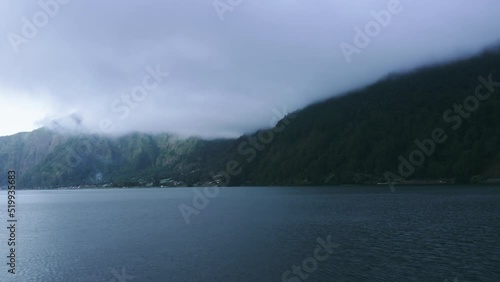 Wallpaper Mural Flying over surface of lake water against background of large mountains shrouded in huge clouds in purple shades of sunset light. A picturesque landscape in motion shot on drone at dusk on Batur lake. Torontodigital.ca