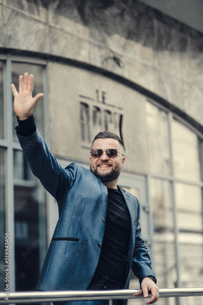 A successful man greets a friend by raising his hand.businessman is waiting for a meeting near the office center.The man greets with gestures. A successful man greets a friend by raising his hand.businessman is waiting for a meeting near the office center.The man greets with gestures.