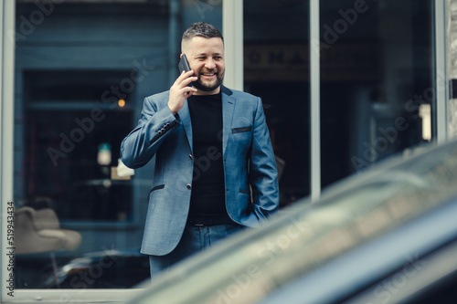 The man waits for a meeting near office. The businessman speaks by phone.Stylish man in a blue suit in the city. Business style of emotion.