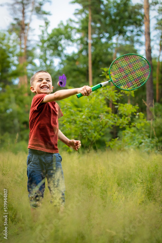 Portrait of little adorable boy playing badminton in meadow in forest in summer