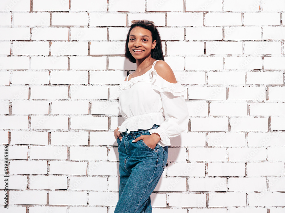 Portrait of young beautiful black woman. Smiling model dressed in summer jeans clothes. Sexy carefree female posing near white brick wall in studio. Tanned and cheerful. In sunglasses Portrait of young beautiful black woman. Smiling model dressed in summer jeans clothes. Sexy carefree female posing near white brick wall in studio. Tanned and cheerful. In sunglasses