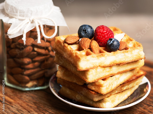 dessert Viennese waffles with almonds raspberries and blueberries on a small plate. jar of almonds