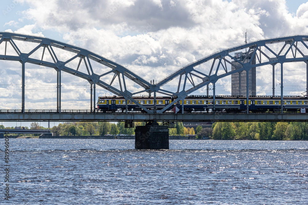Naklejka premium The train rides on the railway bridge against the background of a cloudy blue sky.