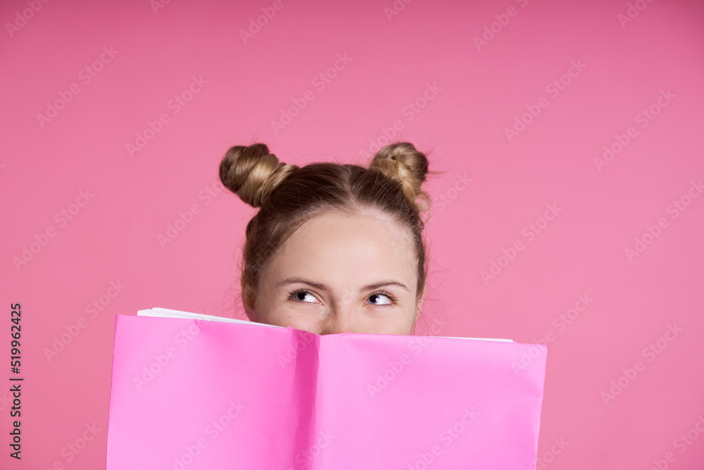 Close up of caucasian female teenager hidden behind pink paper notebook Close up of caucasian female teenager hidden behind pink paper notebook