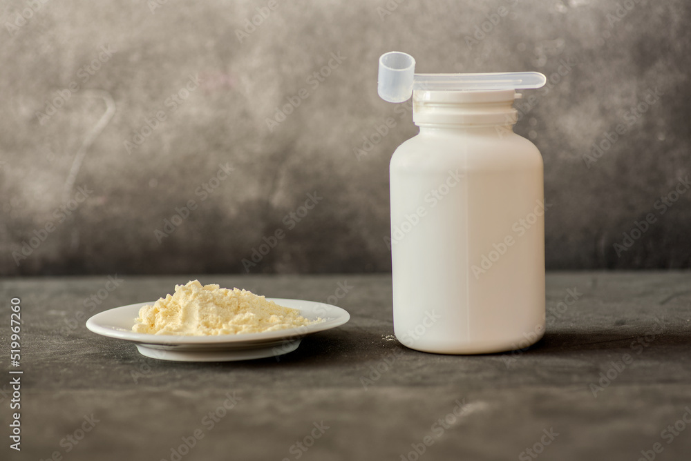 Heap of bovine colostrum powder on plate and white plastic container ...