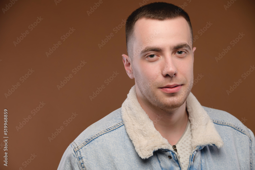 Fototapeta premium A young man in a casual jacket on a brown background looks at the camera and smiles slightly