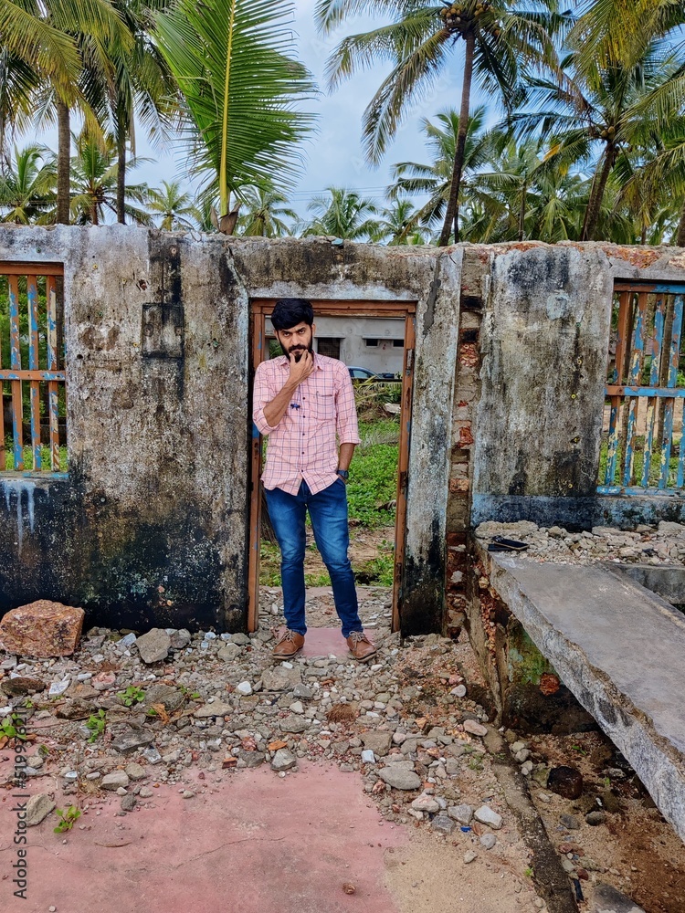  Portrait of a young Indian man well dressed standing near the demolished home under the coconut trees