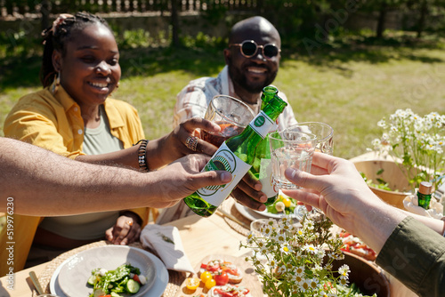 Hands of young interracial friends with glasses of wine and bottles of beer toasting during picnic or outdoor party on summer day