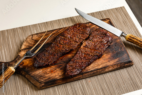 Ready to eat cooked grilled piece of denver steak meat on wooden cutting board with cutlery