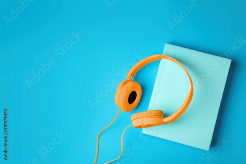 Modern orange headphones with hardcover book on light blue background, top view. Space for text