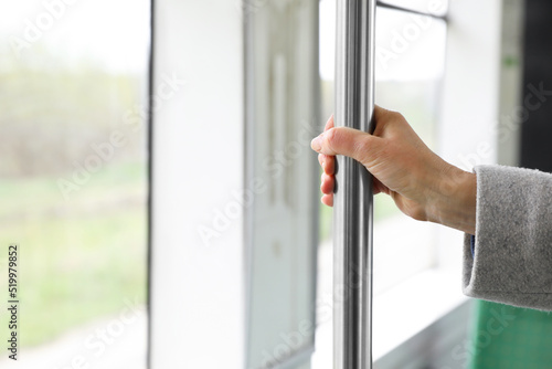 Woman holding grab pole near window in public transport, closeup. Space for text