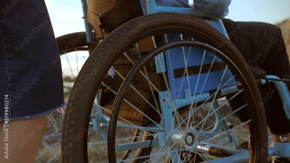 Young man in a wheelchair rides along the beach. Girl drives a disabled ...