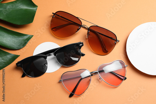 Different stylish sunglasses on pale orange background, flat lay