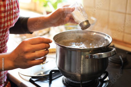 Billede på lærred Woman adding salt to boiling water in pot on stove indoors, closeup
