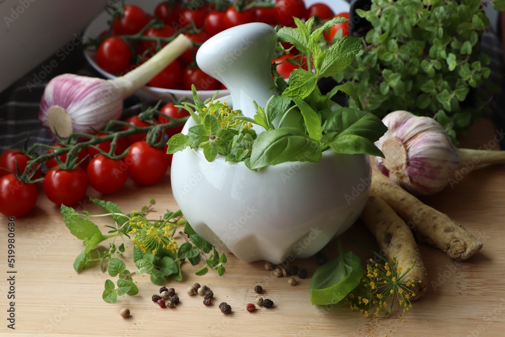 Mortar with fresh herbs near garlic, horseradish roots, black peppercorns and cherry tomatoes on wooden table, closeup Mortar with fresh herbs near garlic, horseradish roots, black peppercorns and cherry tomatoes on wooden table, closeup