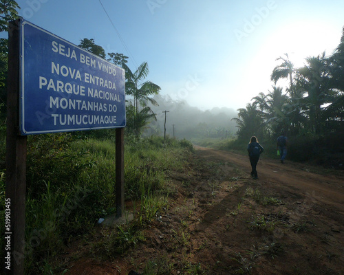 Pessoa mao identificada caminhando ao fundo. Em primeiro plano placa indicando acesso ao parque Nacional Montanhas do tumucumaque, em Pedra branca do Amapari, Amapá photo