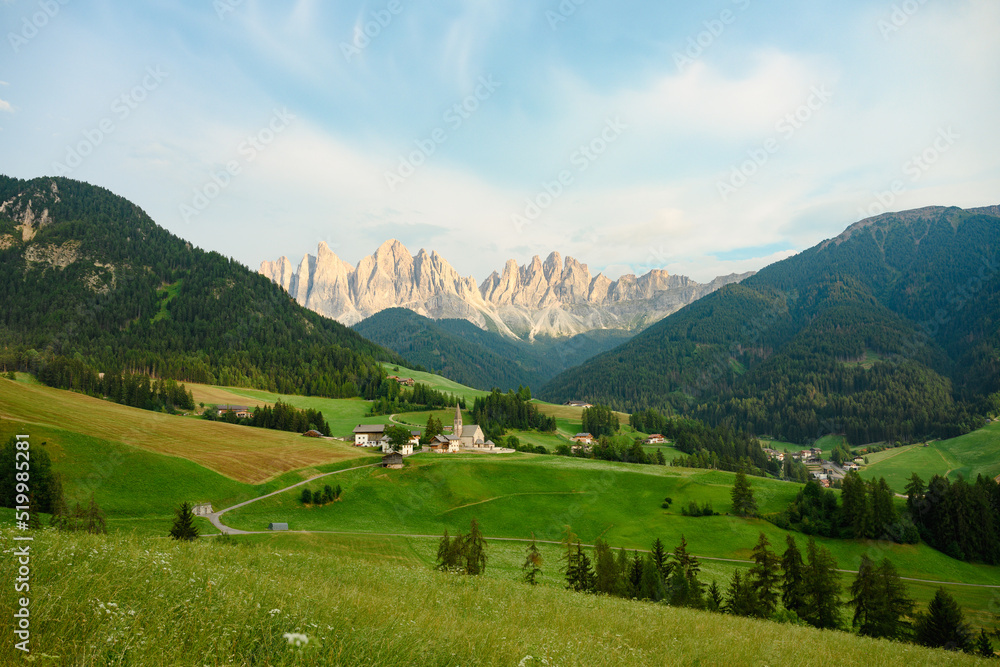 Stunning view of the Funes Valley (Val di Funes) with the Santa Maddalena Church and the mountain range of the Puez Odle Nature Park in the distance during a beautiful sunset. Santa Magdalena, Italy