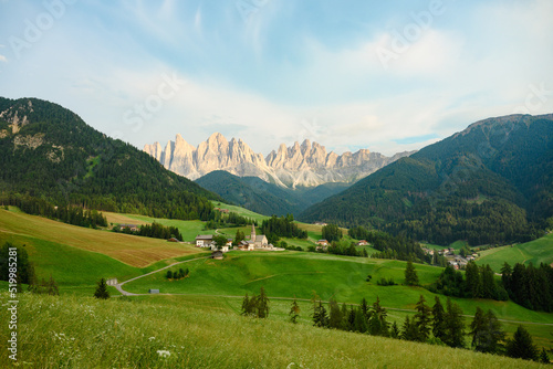 Stunning view of the Funes Valley (Val di Funes) with the Santa Maddalena Church and the mountain range of the Puez Odle Nature Park in the distance during a beautiful sunset. Santa Magdalena, Italy © Travel Wild