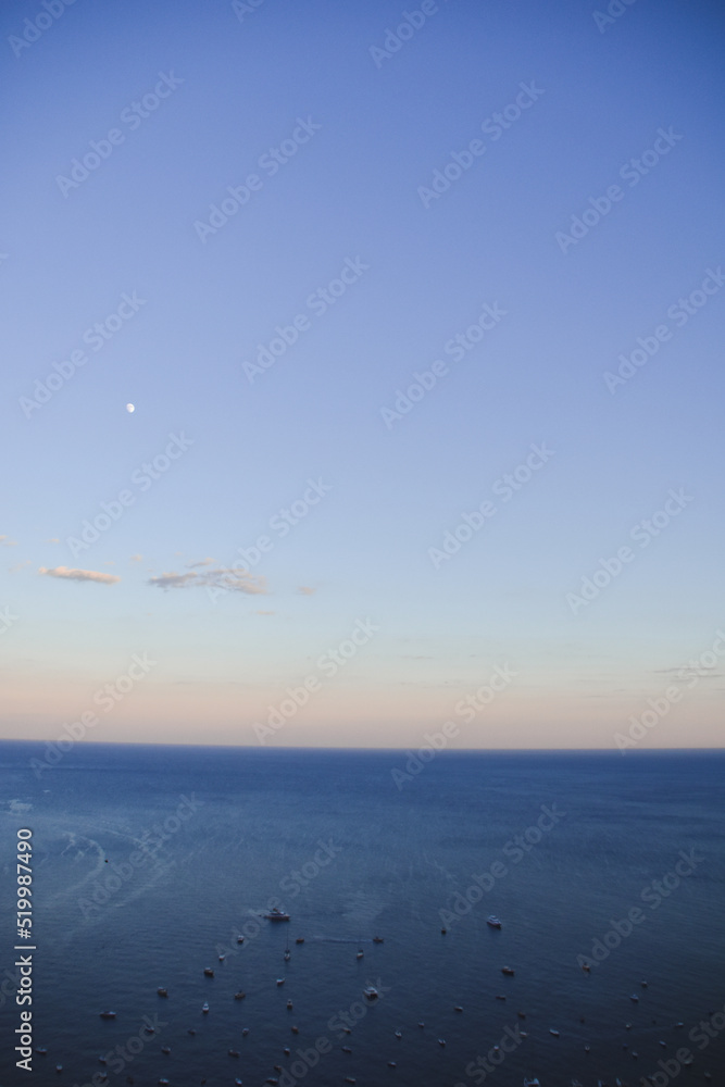 Fotografía vertical de los barcos posicionados en el mar para ver el atardecer desde Positano, Italia.
