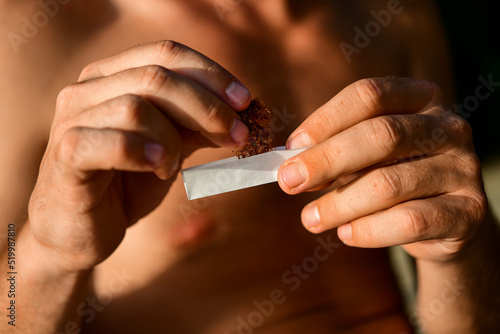Man's hands preparing a tobacco for smoking. Man uses cigarette paper to roll a cigarette 