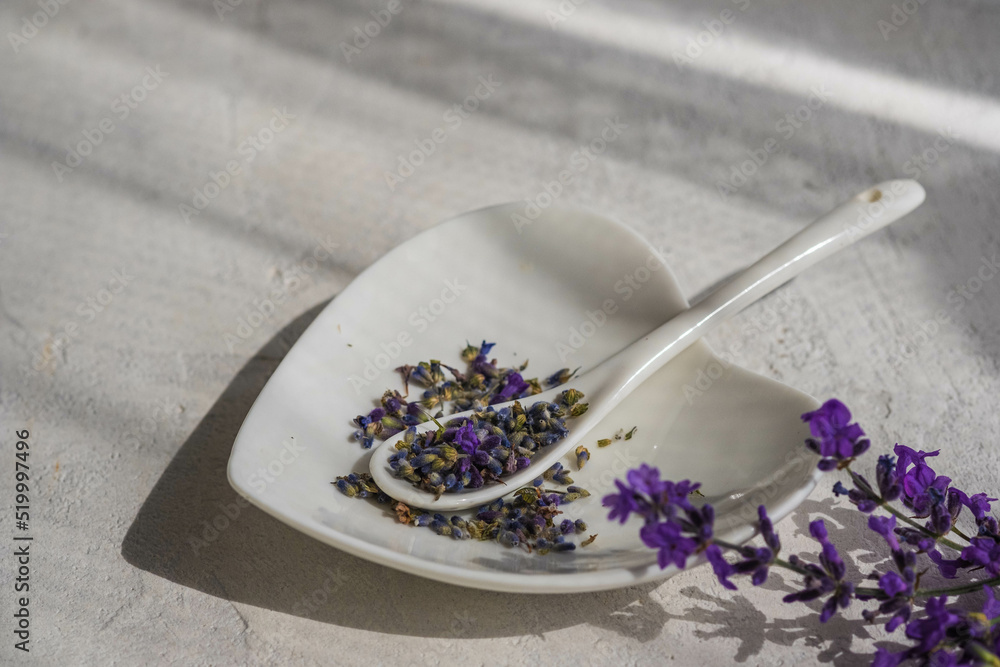 Dried and fresh lavender in a heart-shaped white plate on a light concrete background. Aromatic edible herbs. Dried and fresh lavender in a heart-shaped white plate on a light concrete background. Aromatic edible herbs.