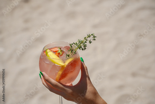 glass of gin and tonic. detail of a woman's hand holding a drink on the beach.