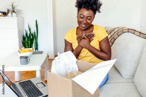 Smiling satisfied African American woman client unboxing parcel. Excited girl removing paper wrap, satisfied client received online store order, good delivery service concept.
