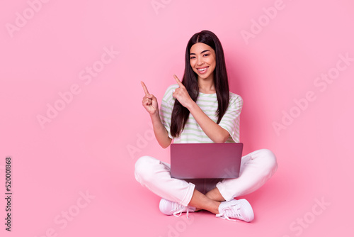 Full body portrait of vietnamese girl sit floor use netbook direct fingers empty space isolated on pink color background