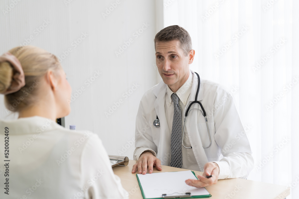 Doctor and female patient. Male doctor discussing and writing note to seek advice problems with woman patient while sitting on the table in the office at the hospital Doctor and female patient. Male doctor discussing and writing note to seek advice problems with woman patient while sitting on the table in the office at the hospital