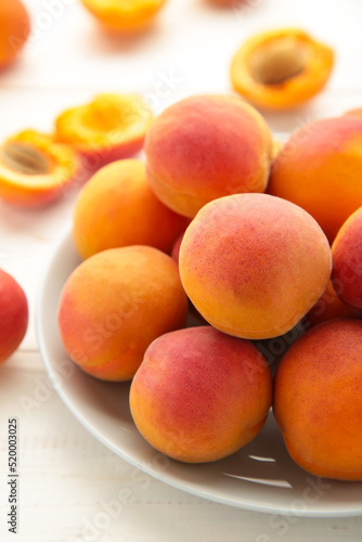 Fresh apricots in the plate on white wooden background. Vertical photo