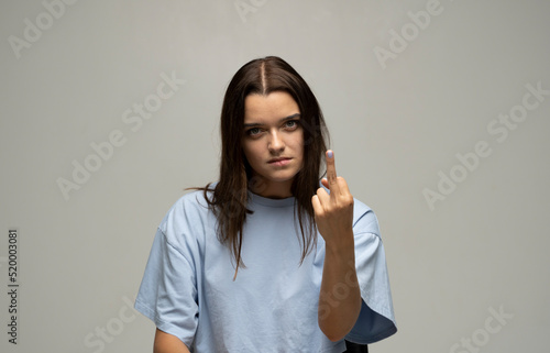 Portrait of crazy angry brunette woman wearing casual style beige t-shirt showing middle finger with one hand, rude gesture, face full of hatred and resentment.