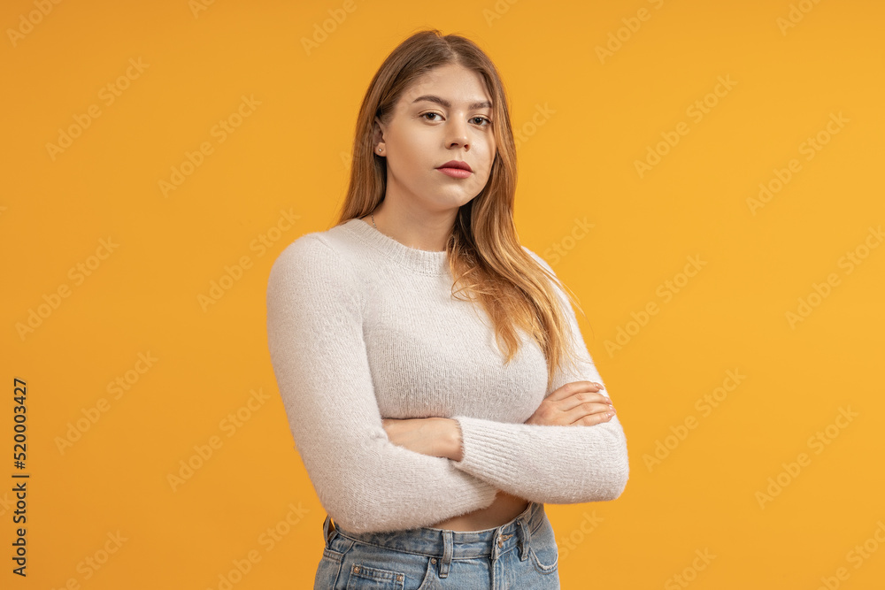 A teenage girl in a tank top and jeans. Arms crossed on chest, arrogant look. Yellow background, half-length portrait. A teenage girl in a tank top and jeans. Arms crossed on chest, arrogant look. Yellow background, half-length portrait.