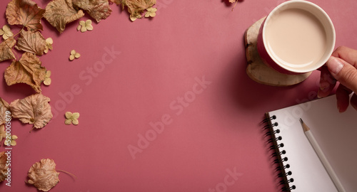 Golden fall autumn leaves, cocoa cup with female hand and note on pink background. Autumn concept, fall background with copy space. Autumn creative composition. Banner