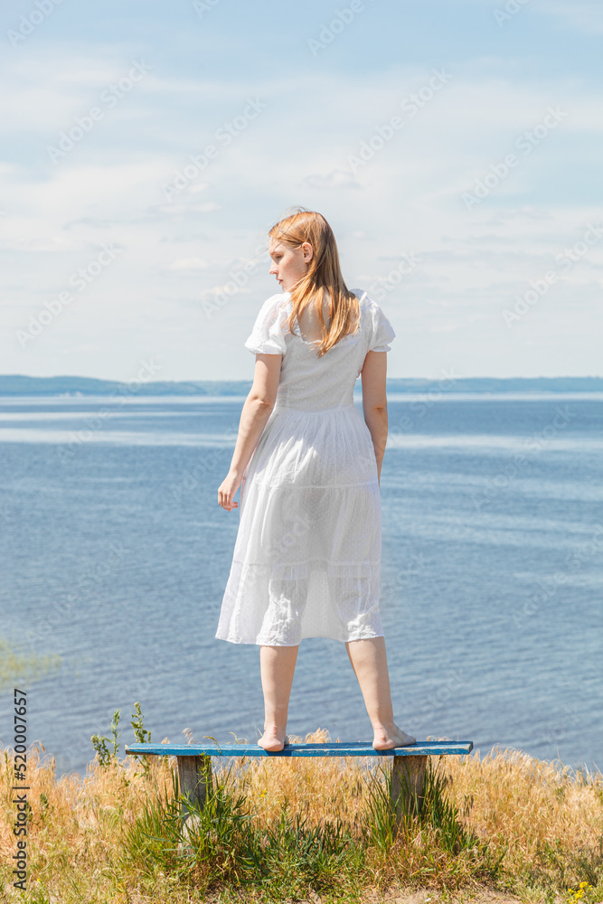 A beautiful girl stands on benches on the seashore with a view of the sky