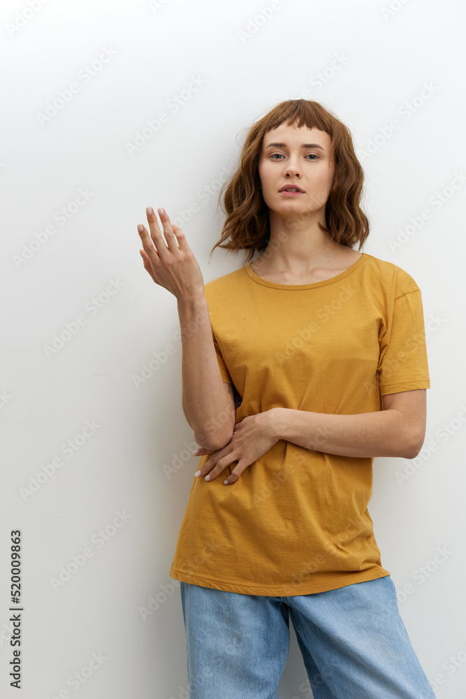 a funny, surprised woman stands on a white background in a yellow cotton T-shirt and poses gesturing with her hands