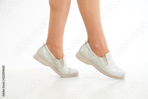 White and silver beautiful fashionable female loafers shoes on leg of girl or woman. Studio shoot on white background for a magazine, website in Internet or catalog