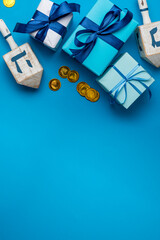 Dreidel, dreidle or dreidl with blue lettering on bright background. Gift box, spinning top, Jewish holiday of Hanukkah, Jewish teetotum, gold coins