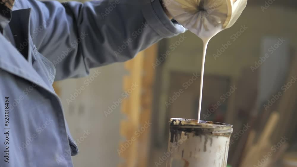 Slow motion. A closeup of a painter pours white varnish into a spray