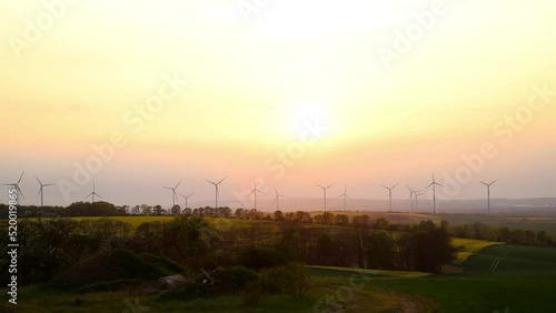 Panoramic landscape view of many modern wind turbine farm power generation station against warm sunset haze mist sky. Clean sustainable zero emission alternative electricity windfarm industry