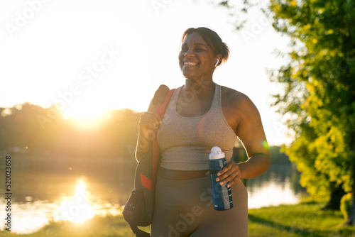 Obraz na płótnie Young African American woman walking with bag and bottle of water through the park in a summer day w salonie