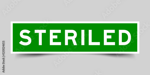 Green color square shape sticker label with word steriled on gray background