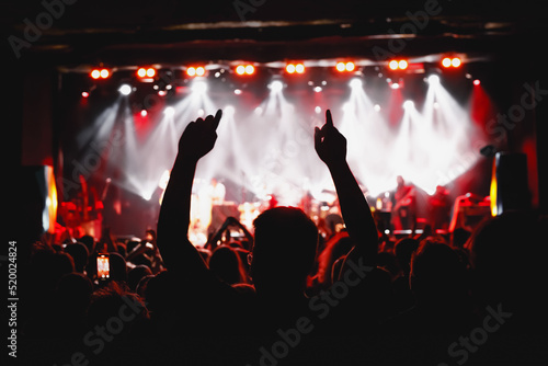 The man with raised hands during the music concert. Crowd and stage light in a concert hall.